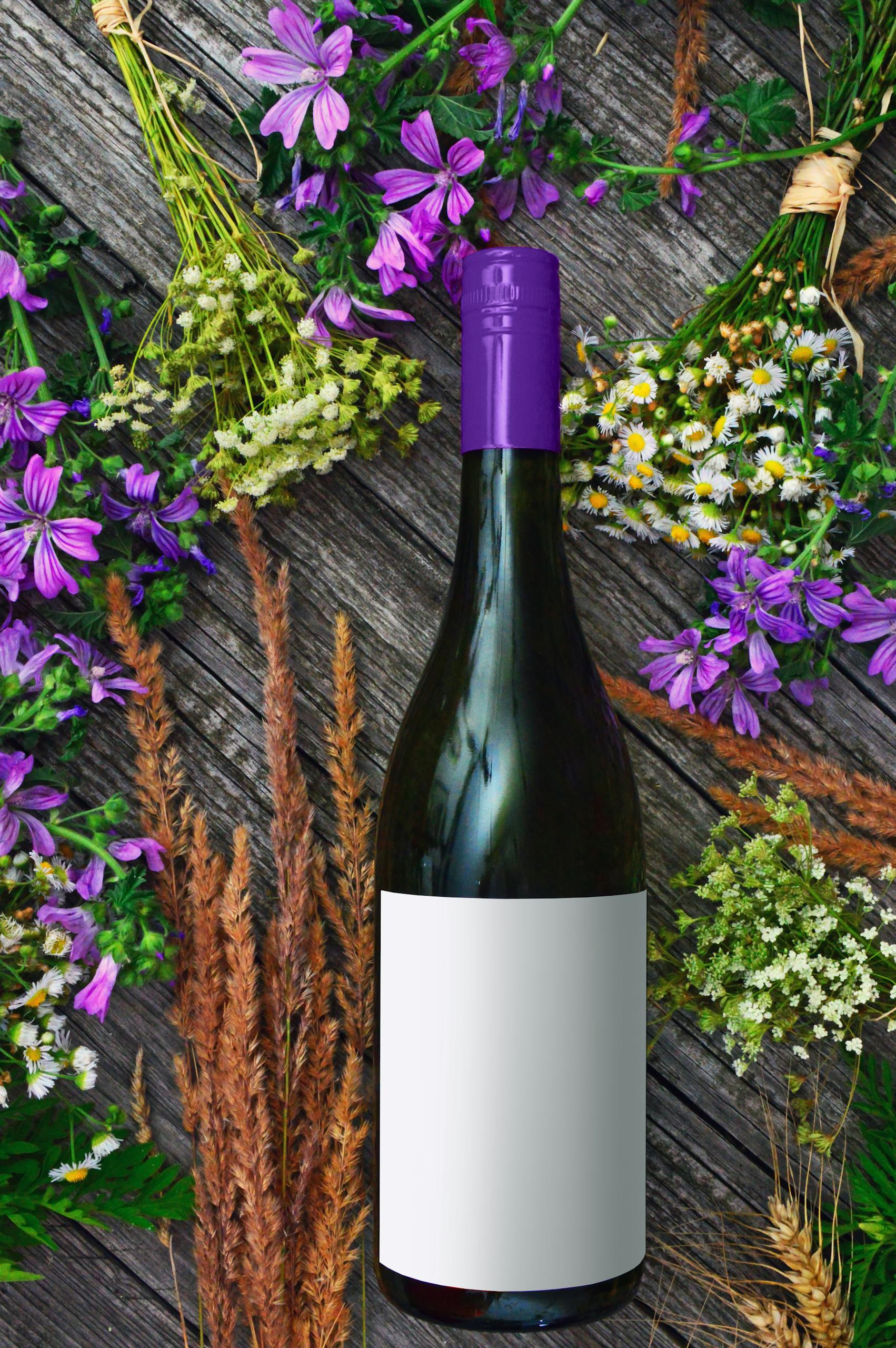 A wine bottle surrounded by vibrant purple flowers and greenery on a rustic wooden surface.