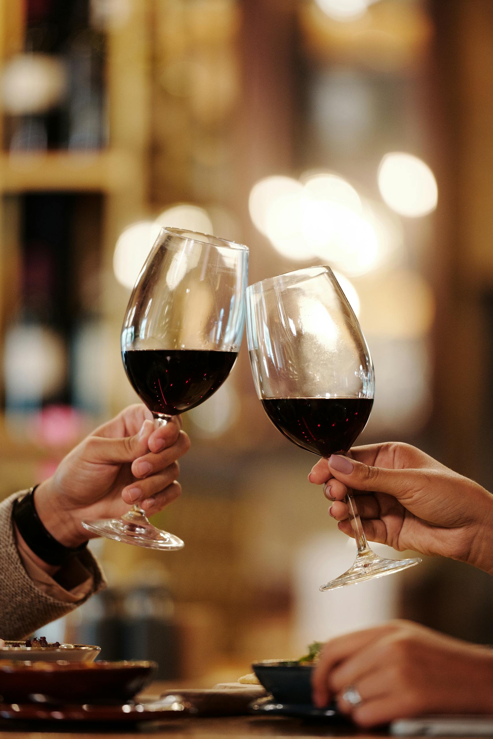 Close-up of two people toasting red wine glasses in a restaurant setting.