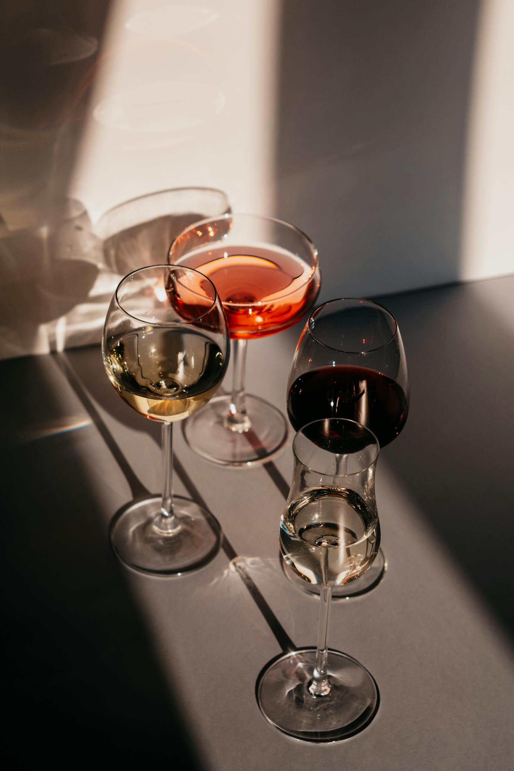 Three wine glasses with red, white, and rosé wine casting shadows in soft lighting.