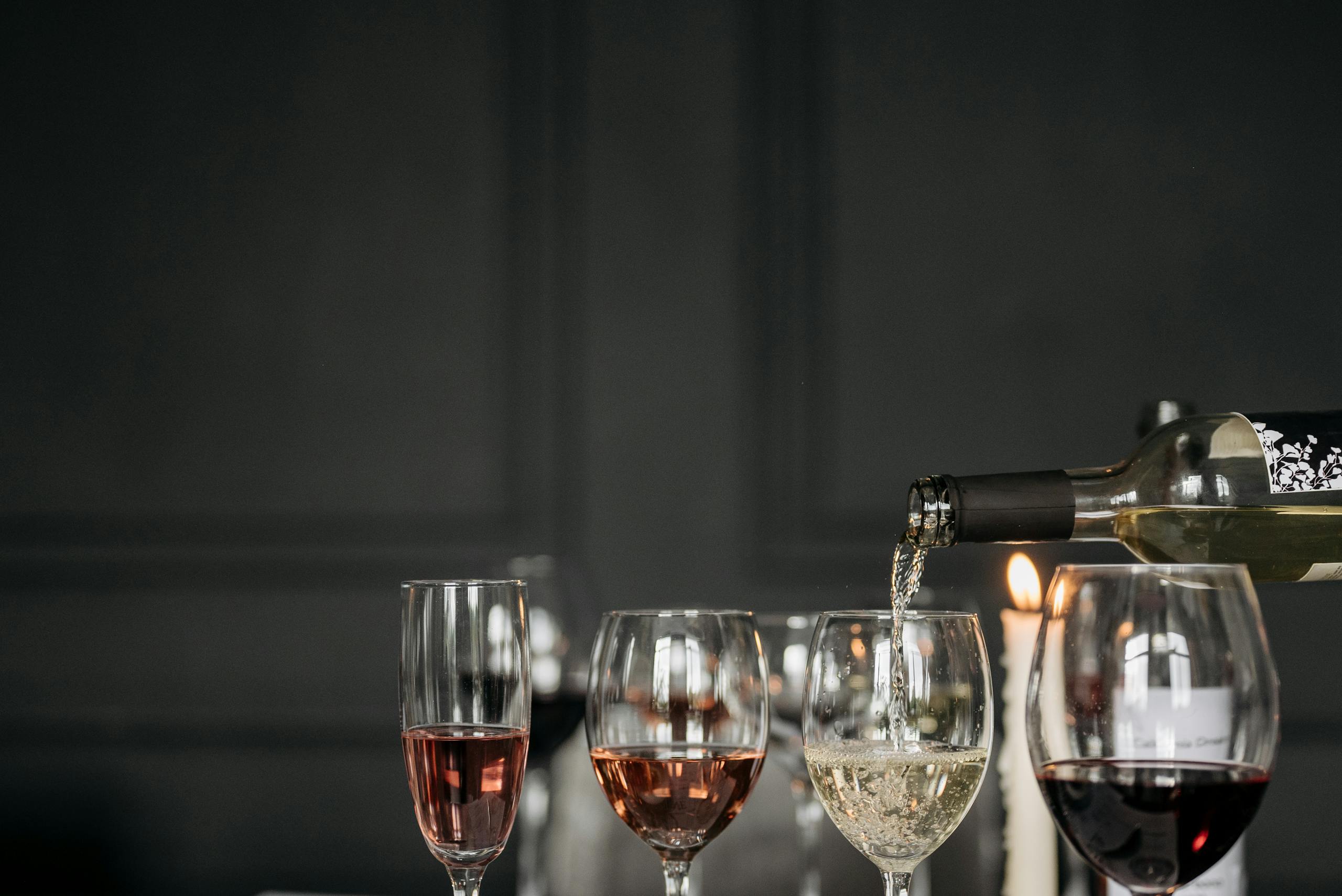 Three wine glasses with red, white, and rosé wine on a dimly lit table setting.